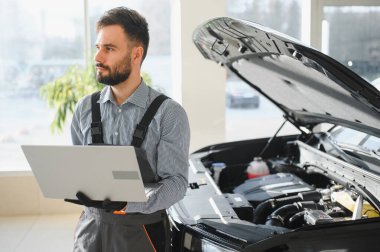 Otomotiv teknisyeni bilgisayarda tanılama yazılımı çalıştırıyor. Tamirci oto servis garajında araç tanılama testi yapıyor..