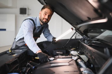 Modern araba tamirhanesinde arabalı dost canlısı bir tamirci. Profesyonel teknisyen araç kontrolü ve bakımını kontrol ediyor. Otomotiv endüstrisi ve müşteri hizmetleri kavramı.