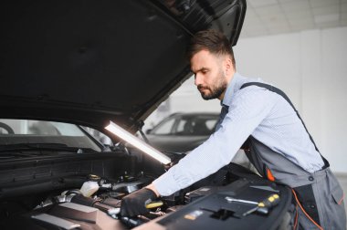 Modern araba tamirhanesinde arabalı dost canlısı bir tamirci. Profesyonel teknisyen araç kontrolü ve bakımını kontrol ediyor. Otomotiv endüstrisi ve müşteri hizmetleri kavramı.