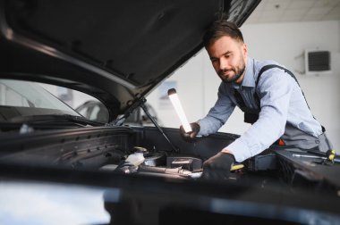 Modern araba tamirhanesinde arabalı dost canlısı bir tamirci. Profesyonel teknisyen araç kontrolü ve bakımını kontrol ediyor. Otomotiv endüstrisi ve müşteri hizmetleri kavramı.