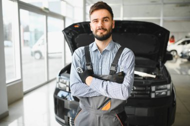 Modern araba tamirhanesinde arabalı dost canlısı bir tamirci. Profesyonel teknisyen araç kontrolü ve bakımını kontrol ediyor. Otomotiv endüstrisi ve müşteri hizmetleri kavramı.