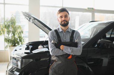 Modern araba tamirhanesinde arabalı dost canlısı bir tamirci. Profesyonel teknisyen araç kontrolü ve bakımını kontrol ediyor. Otomotiv endüstrisi ve müşteri hizmetleri kavramı.
