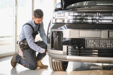 Modern araba tamirhanesinde arabalı dost canlısı bir tamirci. Profesyonel teknisyen araç kontrolü ve bakımını kontrol ediyor. Otomotiv endüstrisi ve müşteri hizmetleri kavramı.