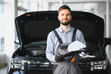 Modern araba tamirhanesinde arabalı dost canlısı bir tamirci. Profesyonel teknisyen araç kontrolü ve bakımını kontrol ediyor. Otomotiv endüstrisi ve müşteri hizmetleri kavramı.