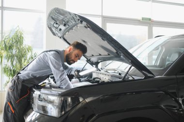 Modern araba tamirhanesinde arabalı dost canlısı bir tamirci. Profesyonel teknisyen araç kontrolü ve bakımını kontrol ediyor. Otomotiv endüstrisi ve müşteri hizmetleri kavramı.