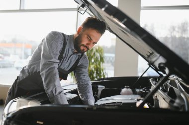 Modern araba tamirhanesinde arabalı dost canlısı bir tamirci. Profesyonel teknisyen araç kontrolü ve bakımını kontrol ediyor. Otomotiv endüstrisi ve müşteri hizmetleri kavramı.