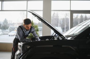 Modern araba tamirhanesinde arabalı dost canlısı bir tamirci. Profesyonel teknisyen araç kontrolü ve bakımını kontrol ediyor. Otomotiv endüstrisi ve müşteri hizmetleri kavramı.