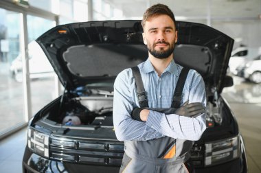 Modern araba tamirhanesinde arabalı dost canlısı bir tamirci. Profesyonel teknisyen araç kontrolü ve bakımını kontrol ediyor. Otomotiv endüstrisi ve müşteri hizmetleri kavramı.