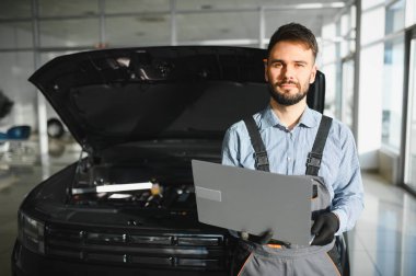 Otomotiv teknisyeni bilgisayarda tanılama yazılımı çalıştırıyor. Tamirci oto servis garajında araç tanılama testi yapıyor..
