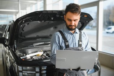 Otomotiv teknisyeni bilgisayarda tanılama yazılımı çalıştırıyor. Tamirci oto servis garajında araç tanılama testi yapıyor..