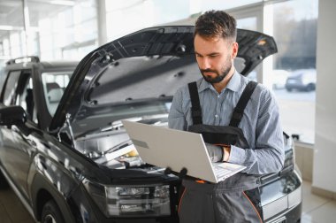 Modern araba tamirhanesinde arabalı dost canlısı bir tamirci. Profesyonel teknisyen araç kontrolü ve bakımını kontrol ediyor. Otomotiv endüstrisi ve müşteri hizmetleri kavramı.