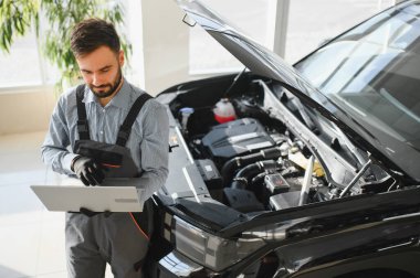 Modern araba tamirhanesinde arabalı dost canlısı bir tamirci. Profesyonel teknisyen araç kontrolü ve bakımını kontrol ediyor. Otomotiv endüstrisi ve müşteri hizmetleri kavramı.