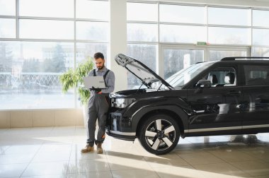 Otomotiv teknisyeni bilgisayarda tanılama yazılımı çalıştırıyor. Tamirci oto servis garajında araç tanılama testi yapıyor..
