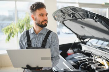 Modern araba tamirhanesinde arabalı dost canlısı bir tamirci. Profesyonel teknisyen araç kontrolü ve bakımını kontrol ediyor. Otomotiv endüstrisi ve müşteri hizmetleri kavramı.