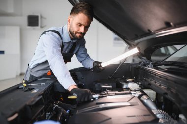 Modern araba tamirhanesinde arabalı dost canlısı bir tamirci. Profesyonel teknisyen araç kontrolü ve bakımını kontrol ediyor. Otomotiv endüstrisi ve müşteri hizmetleri kavramı.