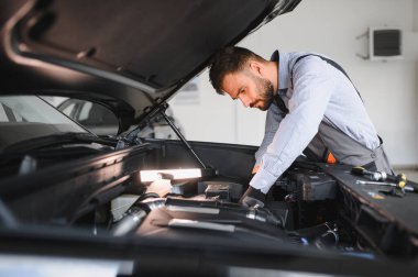 Modern araba tamirhanesinde arabalı dost canlısı bir tamirci. Profesyonel teknisyen araç kontrolü ve bakımını kontrol ediyor. Otomotiv endüstrisi ve müşteri hizmetleri kavramı.
