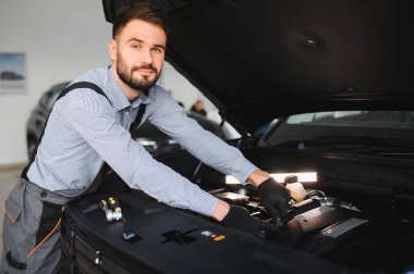 Modern araba tamirhanesinde arabalı dost canlısı bir tamirci. Profesyonel teknisyen araç kontrolü ve bakımını kontrol ediyor. Otomotiv endüstrisi ve müşteri hizmetleri kavramı.