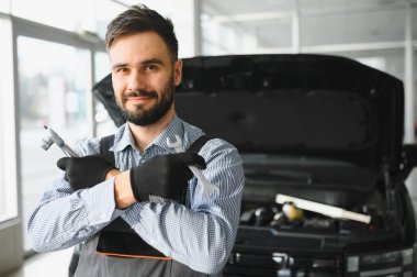 Modern araba tamirhanesinde arabalı dost canlısı bir tamirci. Profesyonel teknisyen araç kontrolü ve bakımını kontrol ediyor. Otomotiv endüstrisi ve müşteri hizmetleri kavramı.