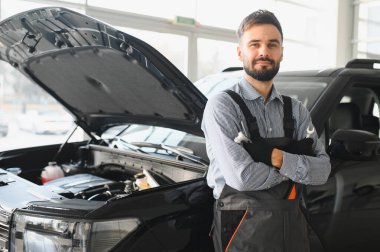 Modern araba tamirhanesinde arabalı dost canlısı bir tamirci. Profesyonel teknisyen araç kontrolü ve bakımını kontrol ediyor. Otomotiv endüstrisi ve müşteri hizmetleri kavramı.
