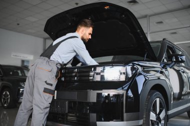 Modern araba tamirhanesinde arabalı dost canlısı bir tamirci. Profesyonel teknisyen araç kontrolü ve bakımını kontrol ediyor. Otomotiv endüstrisi ve müşteri hizmetleri kavramı.