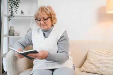 Huzurlu, olgun bir kadın kitap okuyor, favori edebiyat, son sınıf bayan dinleniyor, boş vakitlerin tadını çıkarıyor, hafta sonu evde..