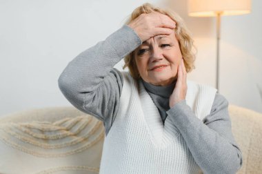 Şakaklarına masaj yapan yaşlı bir kadın baş ağrısı ya da migren konsepti hisseden yaşlı, üzgün, yaşlı, ağrılı ve başı dönen yaşlı bir kadın..