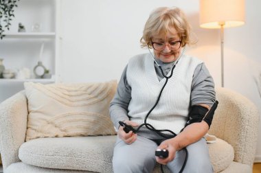 Yüksek tansiyon. Olgun kadın kan basıncını evde tonometreyle ölçüyor, boş alanı olan bir panorama..