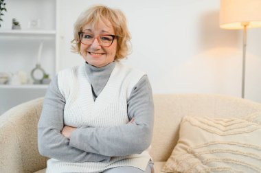 Evde sandalyeye oturmuş gülümseyen olgun bir kadının portresi..