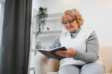 Çekici, rahat, son sınıf öğrencisi bir kadın evinde oturmuş kitap okuyor. Yaşlı, gülümseyen beyaz kadın emeklilikten zevk alıyor..