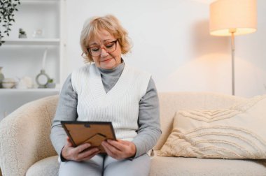 Bunalımlı yaşlı bunak, nostaljisi olan ailesinin fotoğrafına bakıyor, bunalımlı yaşlı bir kadının elinde resim çerçevesi, tek başına oturuyor..