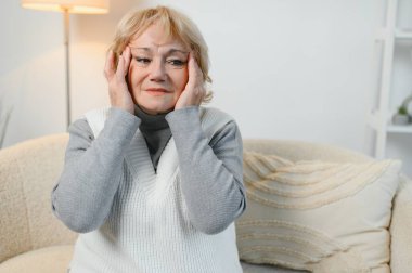 Şakaklarına masaj yapan yaşlı bir kadın baş ağrısı ya da migren konsepti hisseden yaşlı, üzgün, yaşlı, ağrılı ve başı dönen yaşlı bir kadın..