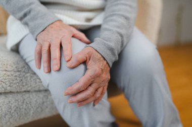 Yaşlı kadın dizini acıdan tutuyor. Yaşlılık, sağlık sorunları ve insanlar konsepti, evde bacağı ağrıyan yaşlı kadın..