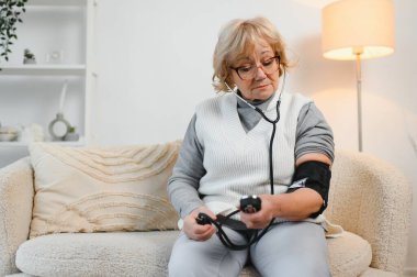 Yaşlı kadın kan basıncını ve kalp atışlarını dijital basınç göstergesiyle kontrol ediyor..