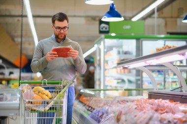 Süpermarkette paketlenmiş çiğ sosis seçen bir adam..