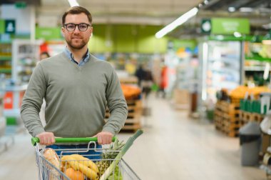 Süpermarketten alışveriş yapan bir adam. Market, alışveriş sepeti. Market ya da süpermarket için adamla pankart. Markette ya da markette yiyecek seçen adam.