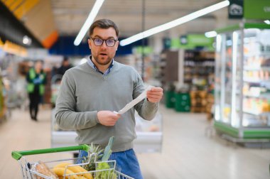 Şok olmuş bir adam marketteki mali faturaya bakıyor..