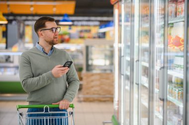 Süpermarketten alışveriş yapan bir adam. Market, alışveriş sepeti. Market ya da süpermarket için adamla pankart. Markette ya da markette yiyecek seçen adam.