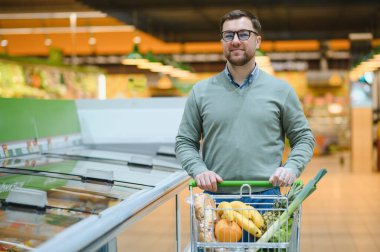 Süpermarketten alışveriş yapan bir adam. Market, alışveriş sepeti. Market ya da süpermarket için adamla pankart. Markette ya da markette yiyecek seçen adam.