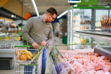 Süpermarkette paketlenmiş çiğ sosis seçen bir adam..
