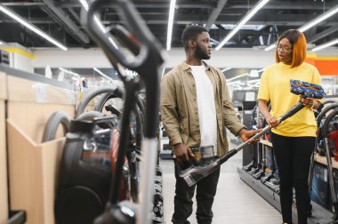Çömelmiş çiftler ve satın almak istedikleri elektrik süpürgesine bakıyorlar. Teknoloji mağazası içi.