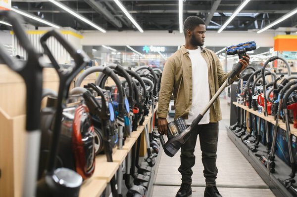 Афроамериканец выбирает новую модель пылесоса в магазине электроники.