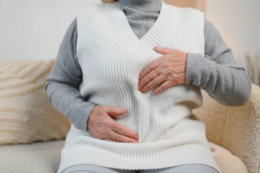 Yatak odasındaki bir yatakta oturan olgun bir kadın mide ağrısı çekiyor. Yatağında oturan yaşlı kadın evinde mide ağrısı çekiyor..