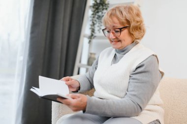 Çekici, rahat, son sınıf öğrencisi bir kadın evinde oturmuş kitap okuyor. Yaşlı, gülümseyen beyaz kadın emeklilikten zevk alıyor..