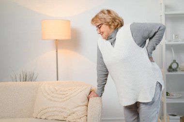 Yaşlı kadın evde sırtı ağrıyor ve sırtına dokunuyor..