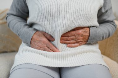 Yatak odasındaki bir yatakta oturan olgun bir kadın mide ağrısı çekiyor. Yatağında oturan yaşlı kadın evinde mide ağrısı çekiyor..