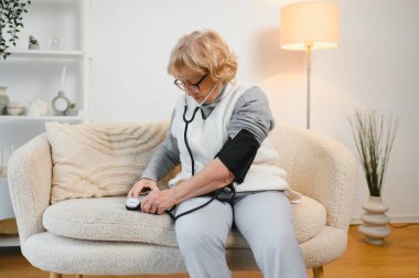 Yüksek tansiyon. Olgun kadın kan basıncını evde tonometreyle ölçüyor, boş alanı olan bir panorama..