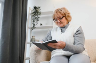 Çekici, rahat, son sınıf öğrencisi bir kadın evinde oturmuş kitap okuyor. Yaşlı, gülümseyen beyaz kadın emeklilikten zevk alıyor..