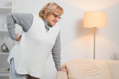 Yaşlı kadın evde sırtı ağrıyor ve sırtına dokunuyor..