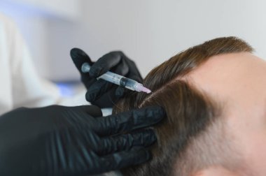 Adam kuaförde kuaförlük yapıyor, mezoterapi seansı yapıyor. Kadın terapist koruyucu eldiven verip şırınga yapıyor..