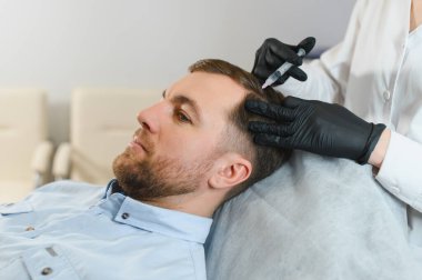 Saç için mezoterapi. Çekici bir adam kafasından iğne vuruluyor. Güzellik salonunda mezoterapi gören bir adam, şırıngalı koruyucu eldivenli bir terapist.,